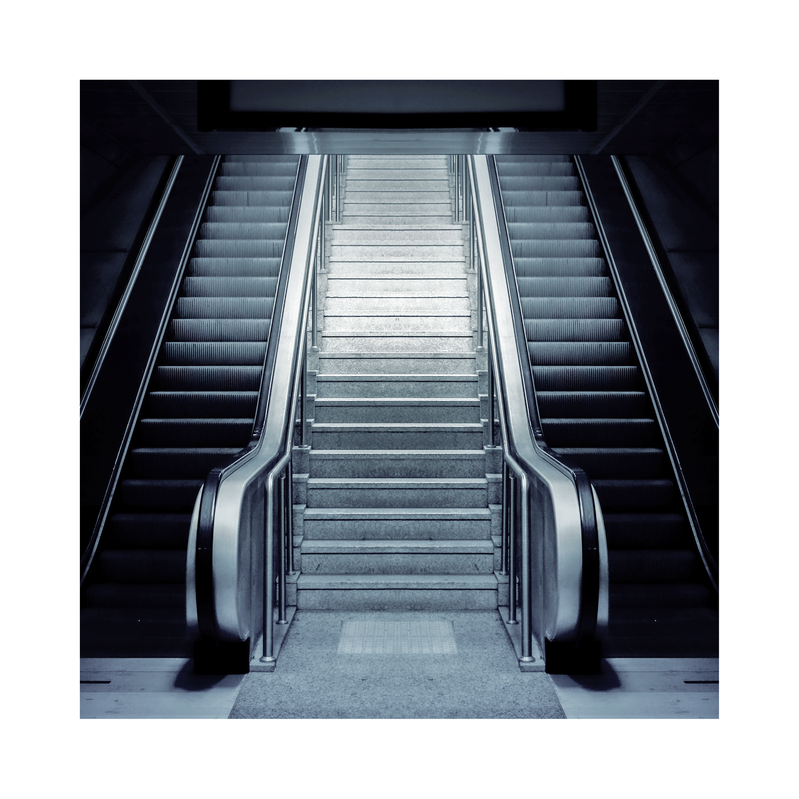 Zdjęcie przedstawia schody ruchome. Widoczne są dwie pary schodów ruchomych po obu stronach szerszych zwykłych schodów.