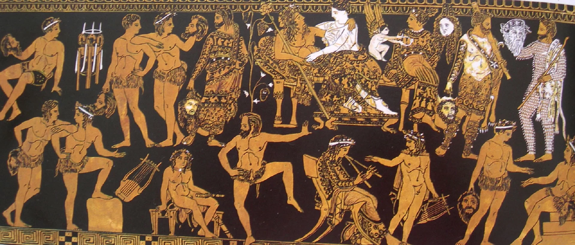 Ilustracja przedstawia fragment naczynia. Waza Pronomosa datowana na V–IV w. p.n.e przedstawiająca trupę aktorską przygotowującą się do przedstawienia. Zdobienia na wazie są koloru złotego, a same naczynie ma kolor brązowy.
