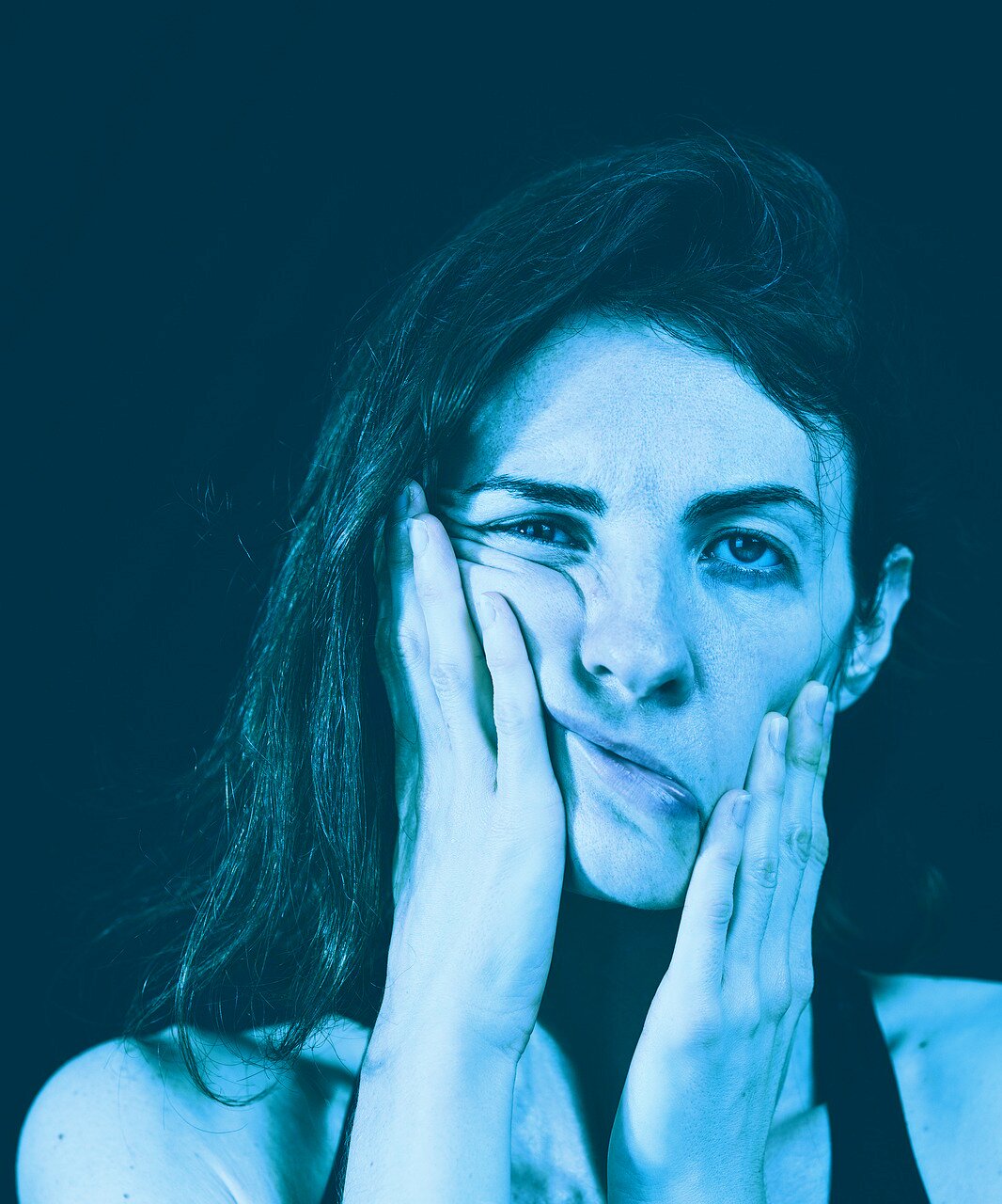 Ilustracja przedstawia smutną kobietę trzymającą się za twarz. Cała ilustracja jest w niebieskich barwach