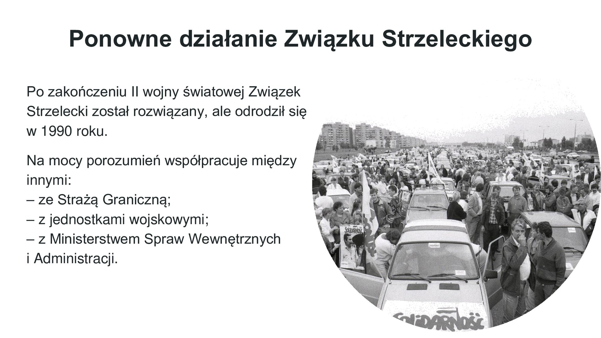 Biały slajd. U góry nagłówek: „Ponowne działanie Związku Strzeleckiego”. Poniżej, z lewej strony, tekst: „Po zakończeniu II wojny światowej Związek Strzelecki został rozwiązany, ale odrodził się w 1990 roku. Na mocy porozumień współpracuje między innymi: ze Strażą Graniczną, z jednostkami wojskowymi, z Ministerstwem Spraw Wewnętrznych i Administracji”. Obok, z prawej strony slajdu, okrągłe, czarno‑białe zdjęcie przedstawiające stare samochody, na maskach których znajduje się napis „Solidarność”. Wokół samochodu tłum ludzi.