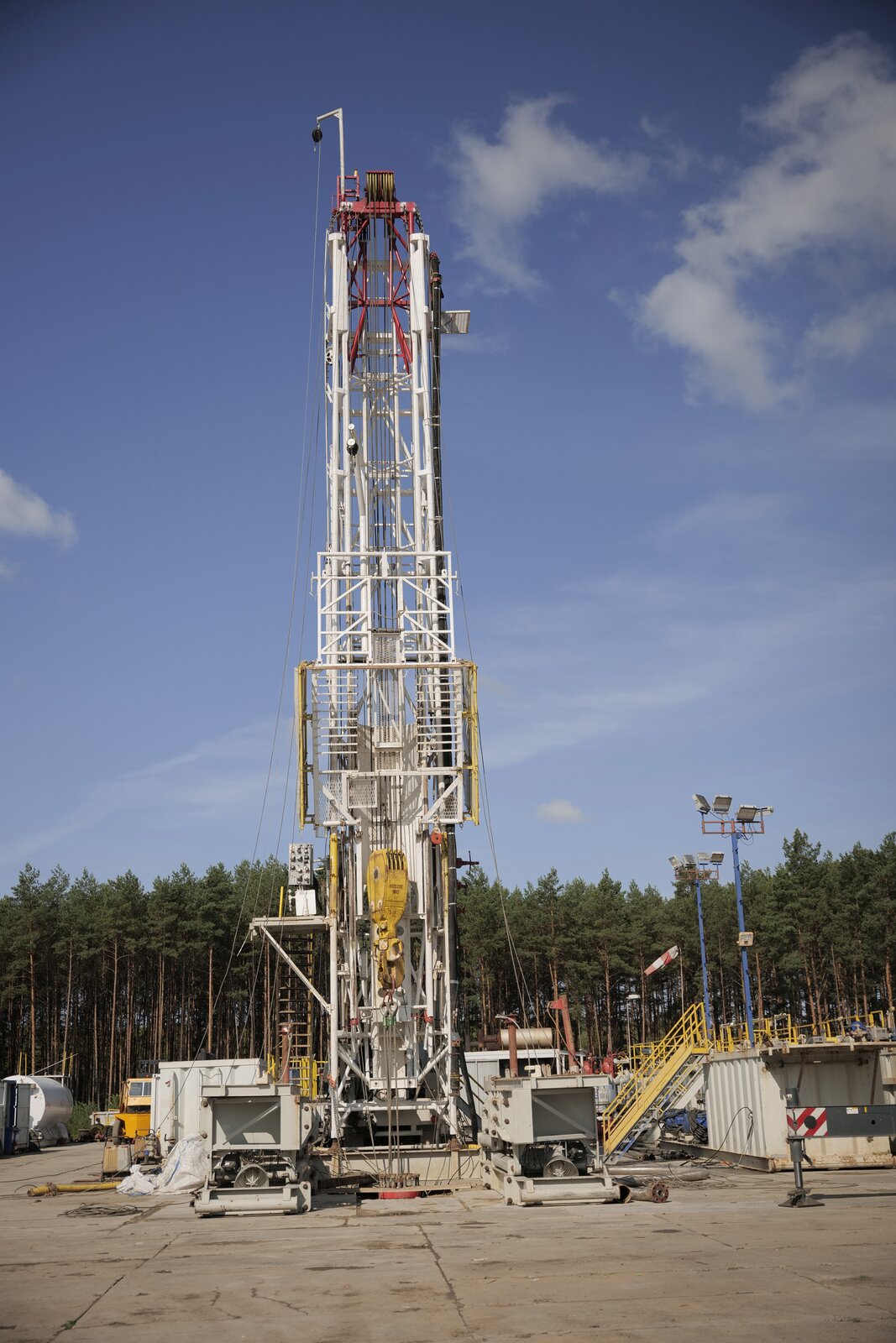 Zdjęcie przedstawia maszt wiertniczy. Stalowa, pionowa kratownica znajdująca się na betonowym podłożu. Na szczycie elementu znajduje się wielokrążek stały.  Z wielokrążka zwisa lina na której,  zawieszony jest żółty hak. Po bokach znajdują się stalowe odciągi linowe.  Masz wiertniczy jest najlżejszym z trzech popularnych kontrukcji nośnych urządzeń wiertniczych. Kratownicowa konstrukcja stawiana do pionu przy pomocy własnych siłowników hydraulicznych. Utrzymywana w pionie przy pomocy odciągów linowych. Urządzenie wyposażone  w maszt jest mobilne,  łatwe i szybkie w montażu.