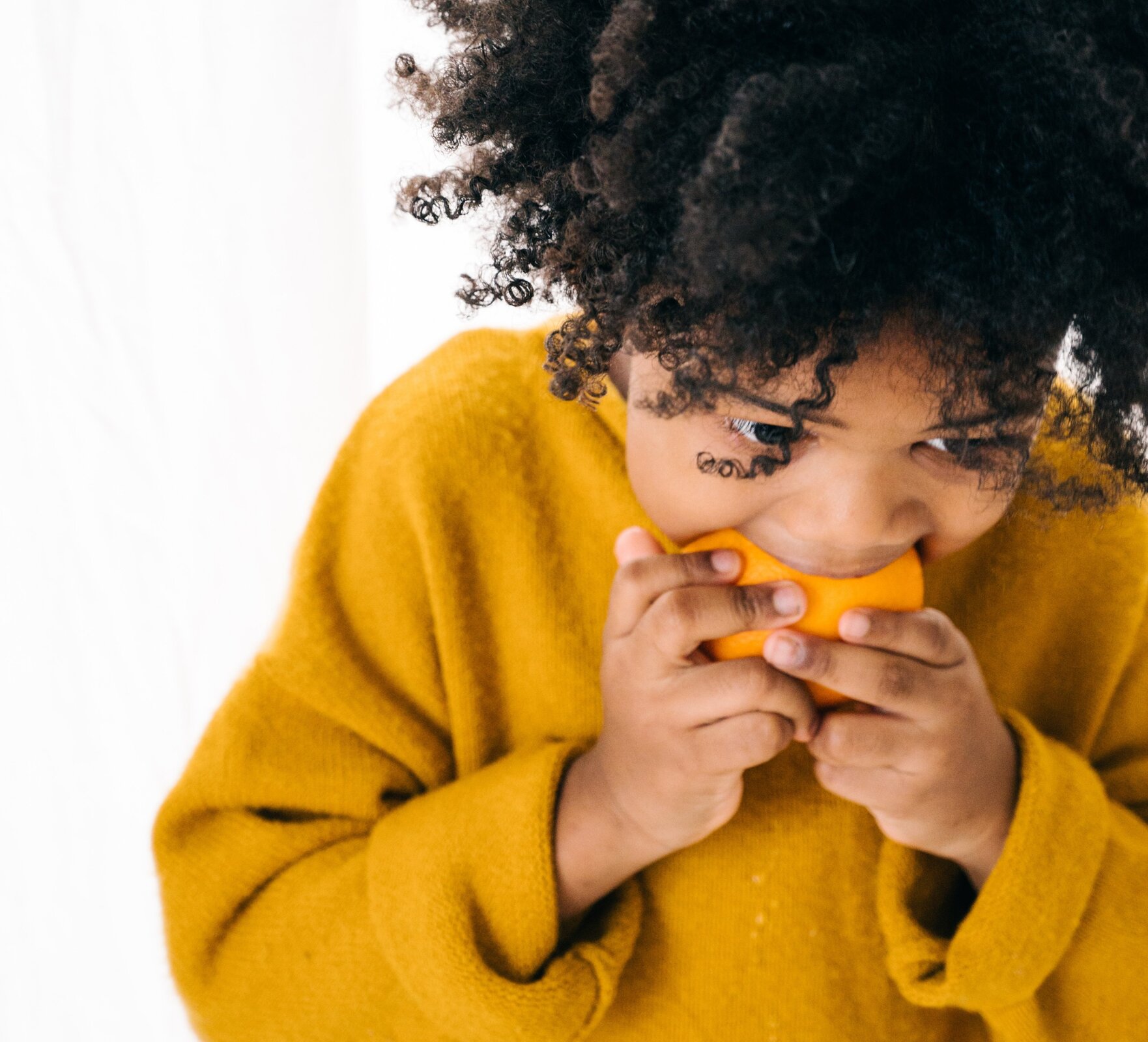 Ilustracja przedstawia dziewczynkę jedzącą pomarańczę.