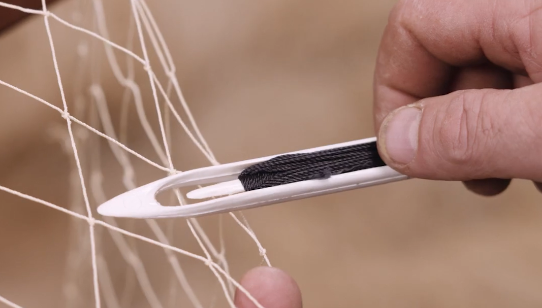 Zdjęcie przedstawia przykładową kleszczkę trzymaną w dłoni. Na kleszczce nawinięta jest nitka, która służy do naprawiania sieci rybackiej. Przednia część kleszczki ma kształt trójkąta, pozostała część przypomina prostokąt.