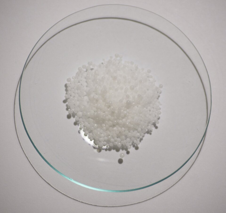 Na ilustracji ukazano szalkę, na której znajduje się stosik drobnych, białych kuleczek.