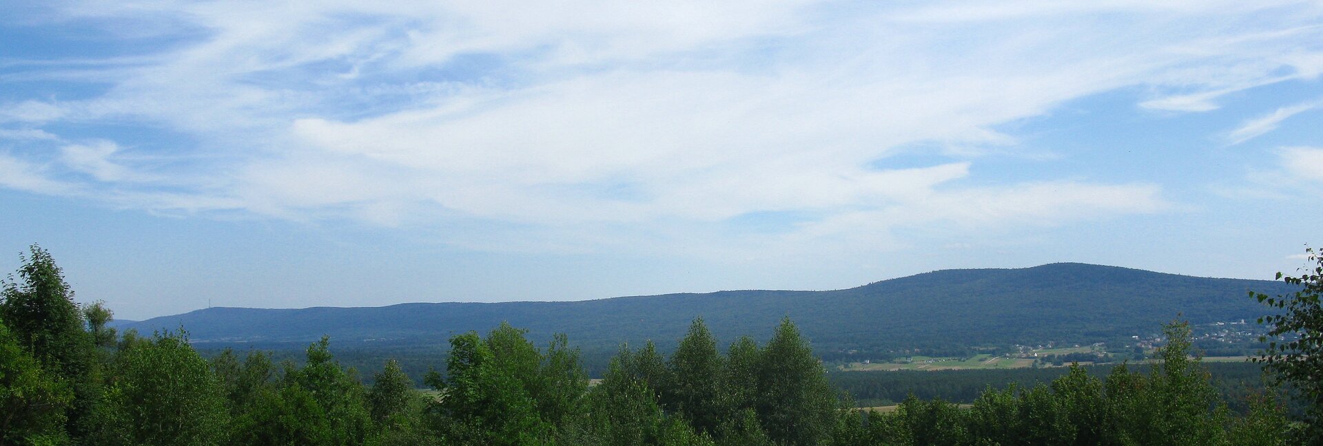 Na zdjęciu na pierwszym planie płaski teren, dalej w tle niskie łegodne góry porośnięte lasami.