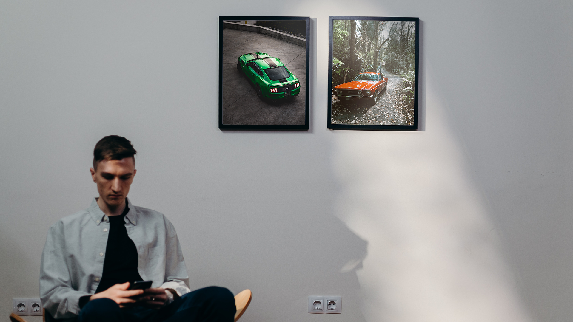 Na zdjęciu chłopak siedzi w pokoju. Na ścianie, za jego plecami wiszą dwa plakaty z samochodami.