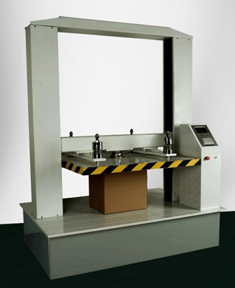 Zdjęcie przedstawia prasę laboratoryjną. Jest to masywne, metalowe urządzenie, które po środku umieszczony ma ciężar oddziałujący na karton, który podlega testowi sprawdzającemu jego wytrzymałość. Po prawej stronie urządzenia znajduje się wyświetlacz wraz z przyciskami funkcyjnymi. 