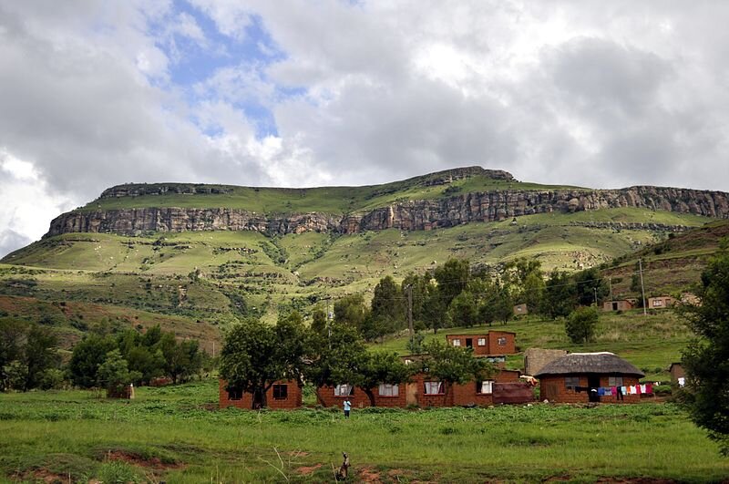 Zdjęcie ukazuje góry zrębowe. Mają one płaski wierzchołek, a poniżej niego uskoki przypominające schody. U podnóża góry stoją niewielkie domy. Teren porasta roślinność - trawa i drzewa.