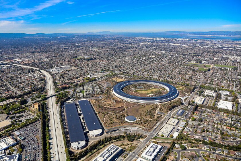 Na ilustracji znajduje się Dolina Krzemowa w USA widoczna z góry. Widać liczne budynki o różnych kształtach rozmieszczone na dużym obszarze. 
