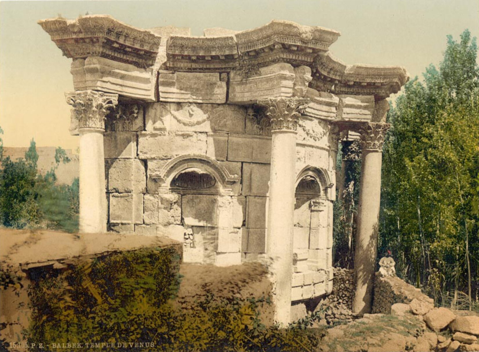 Na zdjęciu ukazano pozostałości świątyni Wenus, znajdujące się w Baalbek. Do naszych czasów zachowała się jedynie część okrągłej ściany oraz kolumny. Kolumny są cztery, nie posiadają żłobień. Na ich szczytach znajdują się bujne zdobienia. Budynek jest zrobiony z białej cegły, na samej górze jest widoczny fragment kopuły. Za świątynią znajdują się drzewa.