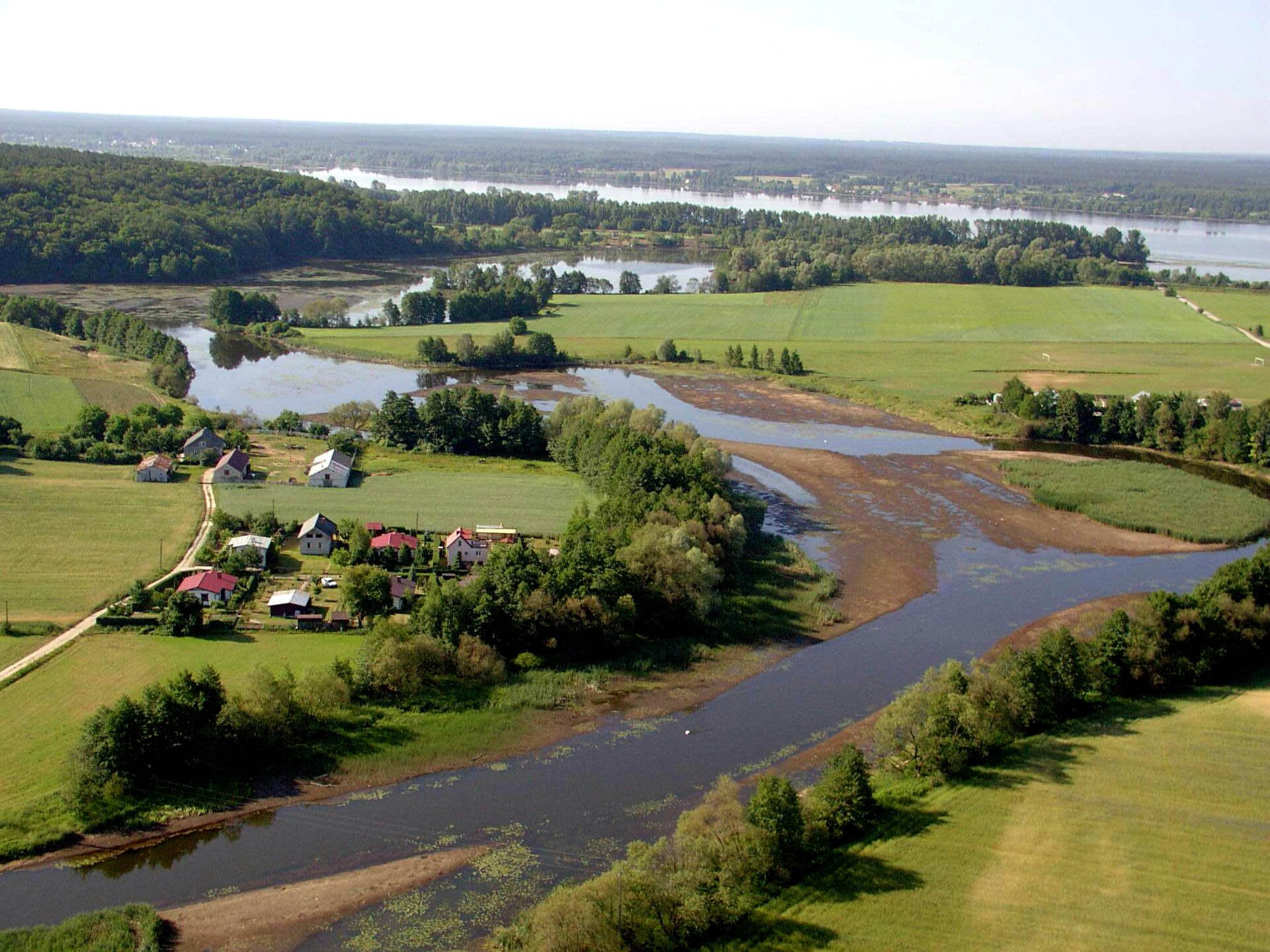 Fotografia przedstawia zdjęcie lotnicze, na nim rozlewisko rzeki, przypominające kształtem literę Y. Po lewej stronie zabudowania, wokół pasowo drzewa. W oddali rozległa rzeka. 