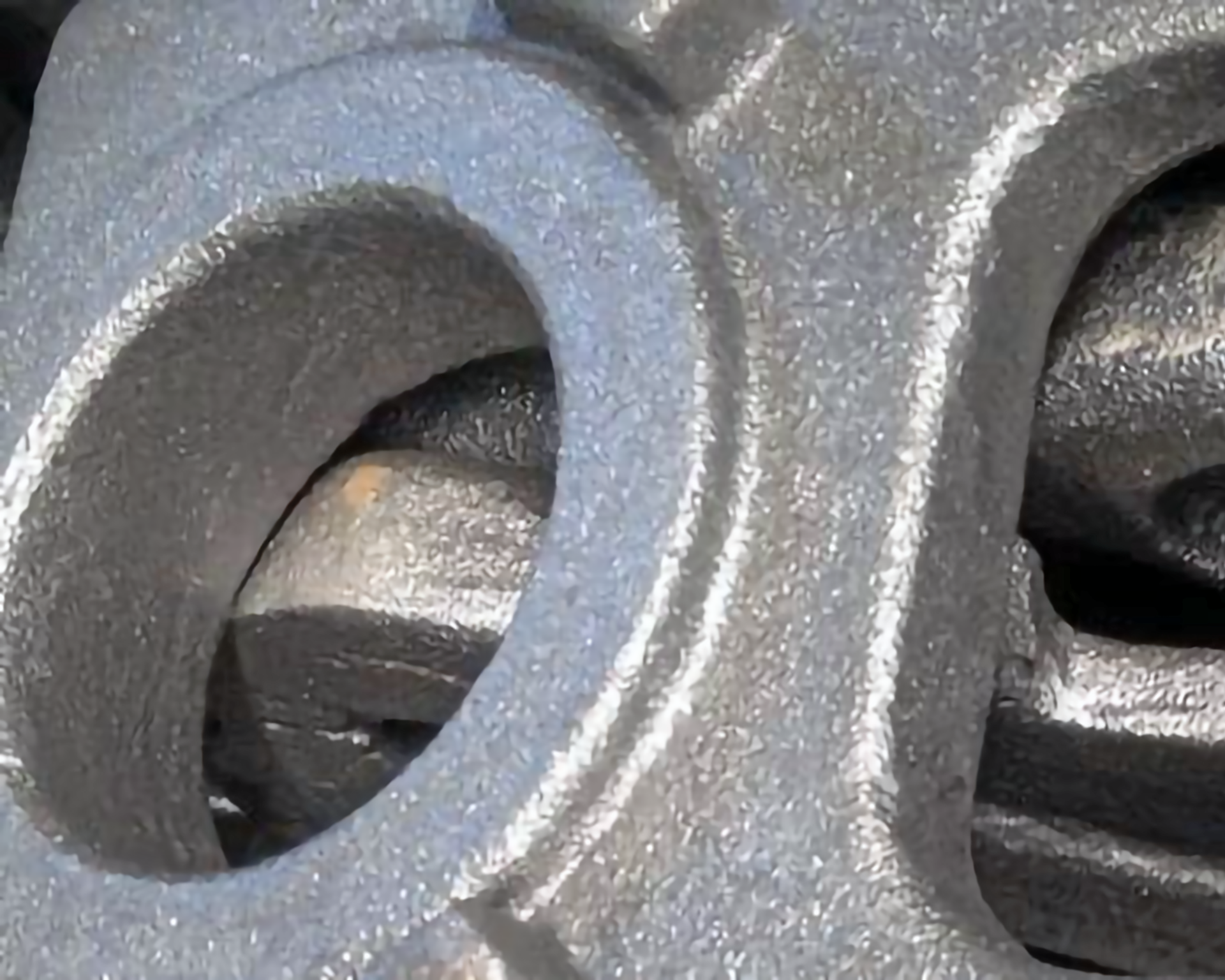 Zdjęcie przedstawia metalowe, płaskie elementy z dużymi dziurami. Powierzchnia tych elementów jest chropowata.