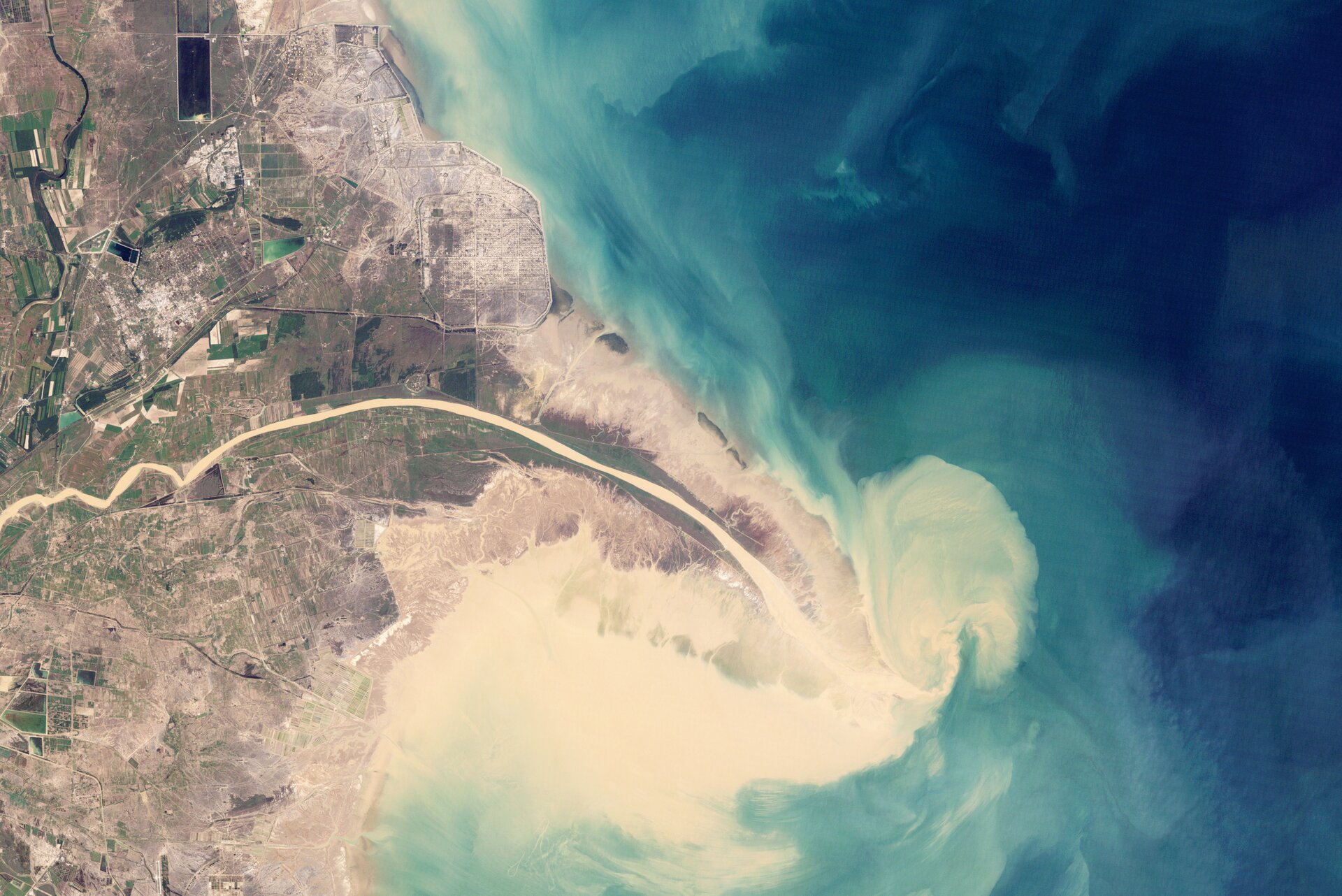 Zdjęcie satelitarne przedstawia deltę rzeki - rzeka ma kolor biały, kontrastuje on z niebieskim kolorem morza.  