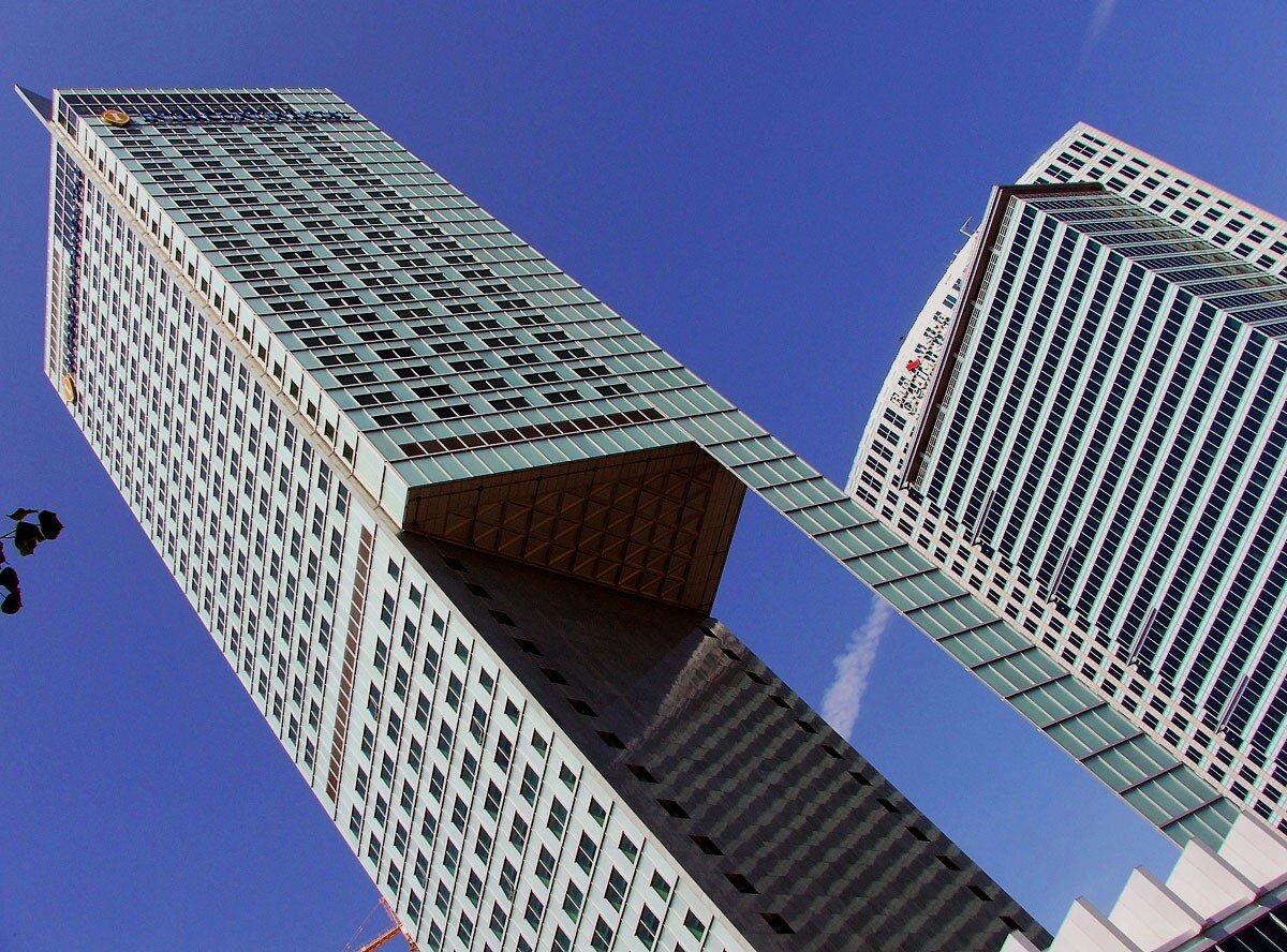 Zdjęcie przedstawia nowoczesne wieżowce, sfotografowane z perspektywy żabiej, z dołu i z ukosa. Ściany budynków mają mnóstwo małych okienek, ustawionych w poziome rzędy. tworzą w ten sposób rytmiczny układ.