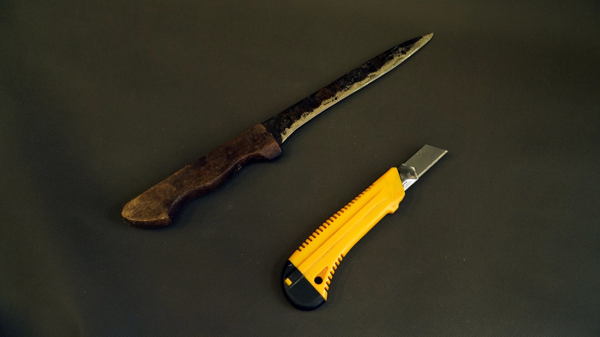 Zdjęcie przedstawia dwa noże. Jeden to klasyczny nóż z metalowym ostrzem i drewnianą rękojeścią, drugi zaś to krótki nożyk o wysuwanym ostrzu umieszczonym w obudowie z tworzywa.