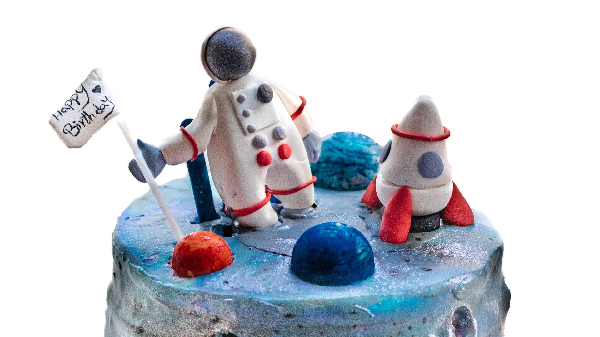 Zdjęcie przedstawia przykładową figurkę z masy cukrowej. Widoczny jest wierzch tortu pokrytego niebieską masą cukrową, na którym widoczne są dwie figurki: kosmonauty trzymającego flagę z napisem Happy Birthday i robota z masy cukrowej oraz kilka półkolistych przedmiotów w kolorze niebieskim, czerwonym i granatowym. Całość symbolizuje lądowanie na księżycu.