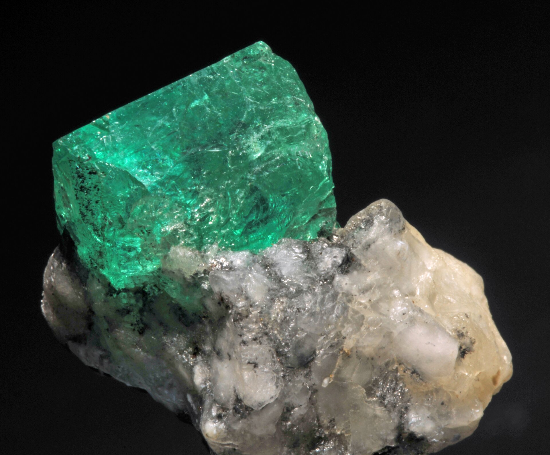 Zdjęcie przedstawia dwa złączone ze sobą minerały - szmaragd i kalcyt. Szmaragd - kryształ o zielonym zabarwieniu, przezroczysty. Kalcyt - biało-szary kamień.