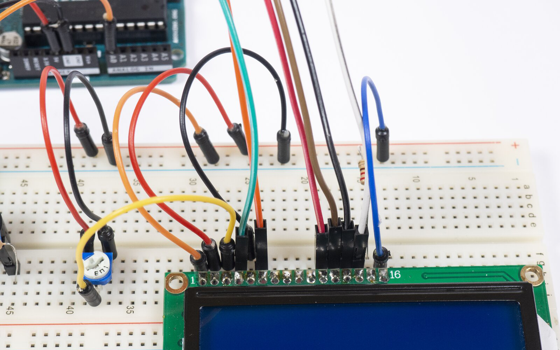 Zdjęcie przedstawia połączenia pomiędzy arduino uno, a płytką stykową. Na płytce znajduje się termometr (względem wycięcia w obudowie) podłączony jest prawą nóżką do uziemienia, lewą do +5V a środkową do pinu A0 arduino. Pin 5V podłączony jest do +5V płytki, a GND podłączone jest do uziemienia. Uziemienie górnej szyny jak i dolnej na płytce stykowej jest połączone. Podłączona jest także LED, jedną nóżką do uziemienia, drugą zaś poprzez rezystor do pinu 7 arduino. Po środku płytki zamontowany jest brzęczyk, który poprzez rezystor łączy się z pinem 6 arduino, a drugą nóżką do uziemienia. Po prawej stronie płytki stykowej podłączono ekran LCD, do którego podłączono kable prowadzące do arduino. Pomiędzy ekranem a brzęczykiem zamontowano potencjometr, do jego nóżek podłączono kable, środkowy do 3 pinu ekranu, lewa nóżka do +5V natomiast prawy do uziemienia. Ostatni i pierwszy pin ekranu podłączono do uziemienia płytki, przedostatni pin podłączono rezystorem do węzła dodatniego płytki. Do 2 pinu ekranu dołączono kabel z węzła dodatniego płytki. Pin 5 ekranu podłączono do szyny dodatniej.