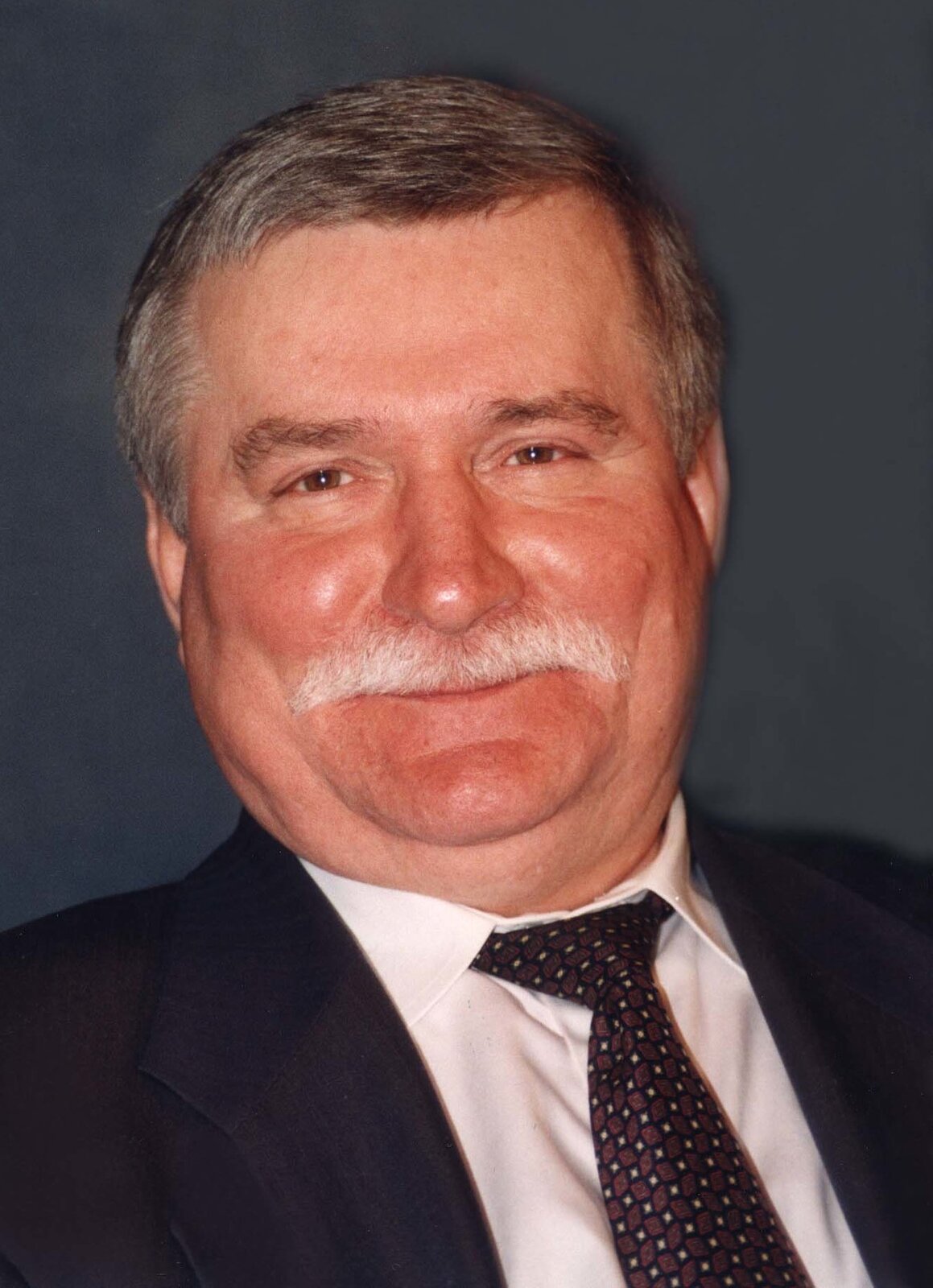 Zdjęcie przedstawia mężczyznę z charakterystycznym wąsem. Jest ubrany w garnitur. To były prezydent Polski Lech Wałęsa. 