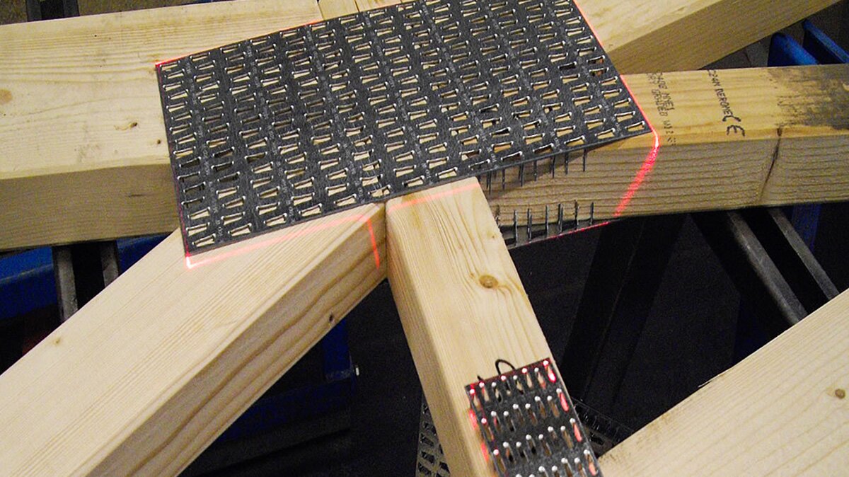 Na zdjęciu widoczne drewniane belki, na nich znajduje się czarna blaszka z licznymi podłużnymi dziurkami. Jest ona przymocowana do belek.