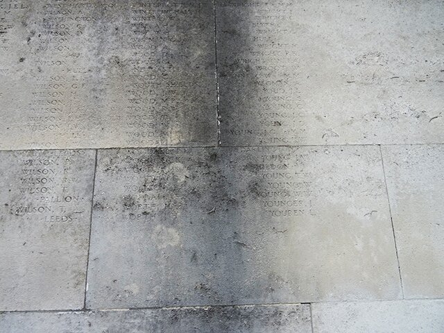 Zdjęcie przedstawia szare płyty. Są na nich częściowo zatarte, niewidoczne napisy.  