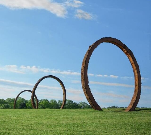 Ilustracja przedstawia rzeźbę  Thomas Sayre  [czytaj: tomasa sejra]. Ukazuje trzy, znajdujące się w znacznej odległości od siebie i postawione na ziemi obręcze o średnicy ok. 5m - są to odlewy ziemne (beton zbrojony tlenkiem żelaza odlany w formach wykopanych z ziemi). W tle znajduje się las. Niebo na fotografii jest pogodne. Na ilustracji umieszczony jest interaktywny punkt z informacją o tytule rzeźby.

