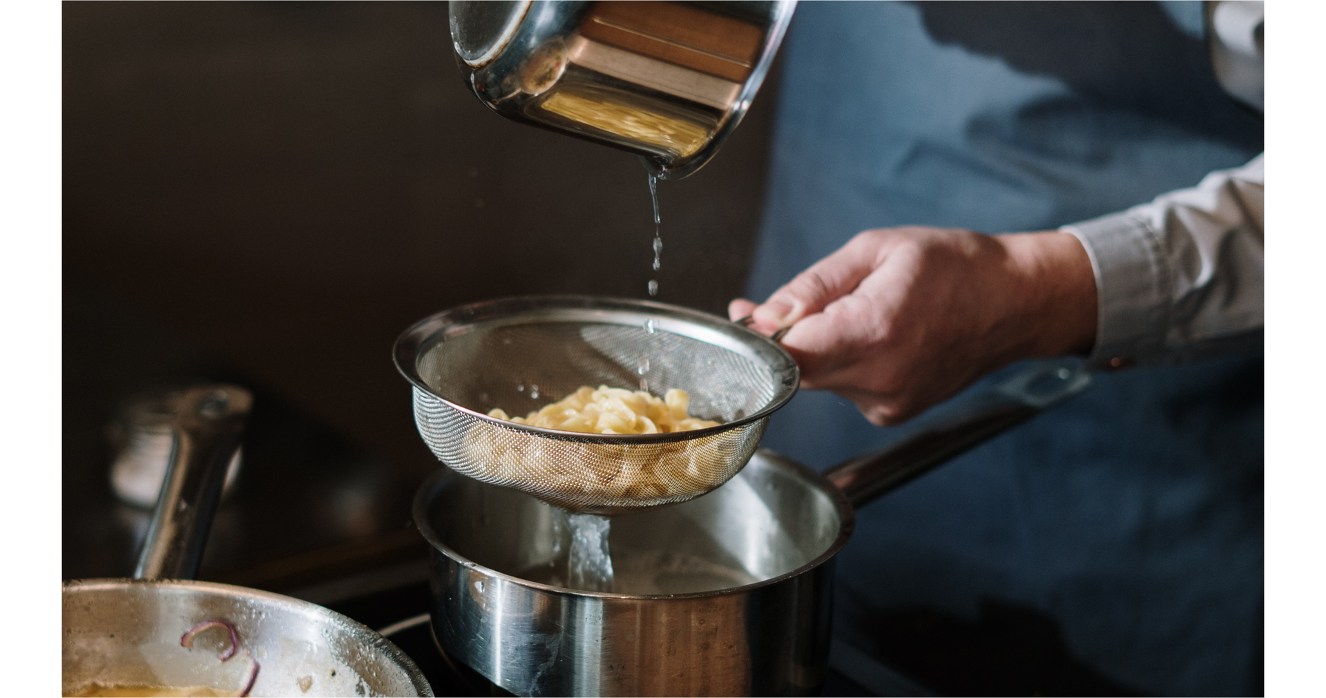 Zdjęcie przedstawia ręce osoby odcedzającej makaron na durszlaku.