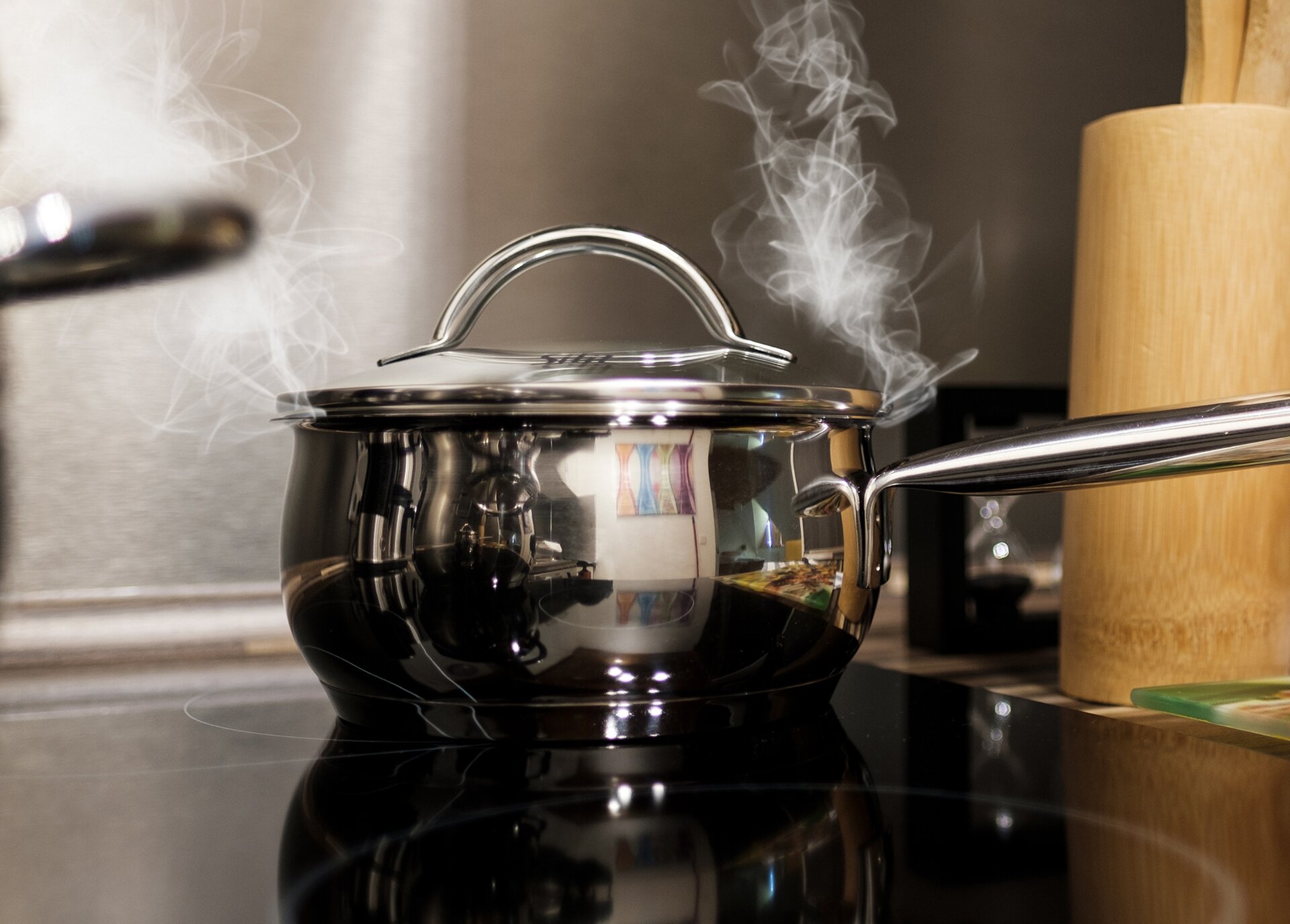 Fot.a. Na zdjęciu jest garnek z gotującą się wodą. Spod pokrywki garnka wydobywa się para.