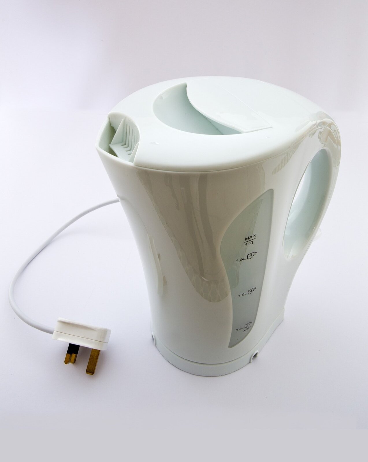 Zdjęcie przedstawia biały czajnik elektryczny stojący na białym blacie kuchennym uchwycony od góry. Na ścianie czajnika widoczna skala pojemności. Wtyczka leży na blacie.