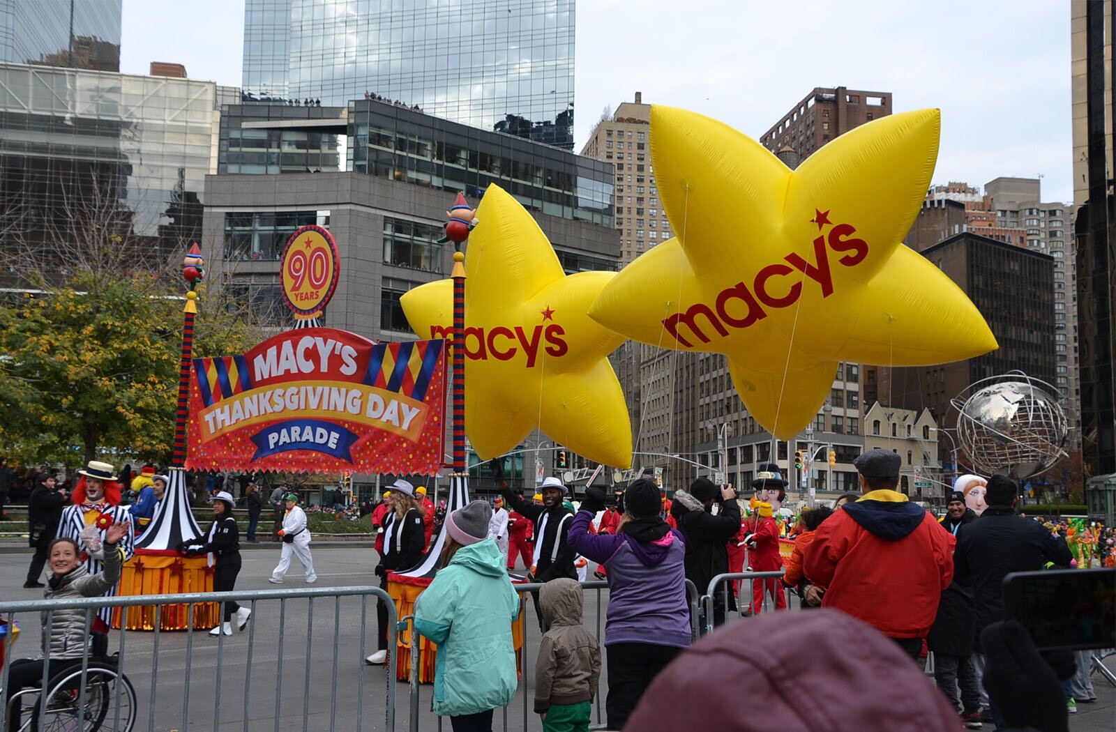 Zdjęcie przedstawia fragment parady gdzie jest niesiony transparent z napisem: "MACY'S THANKSGIVING DAY PARADE". Widzowie stoją za barierkami.