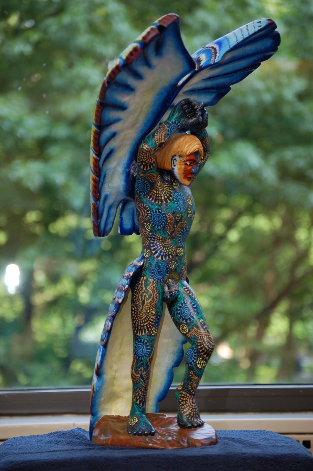 Zdjęcie przedstawia figurkę nagiego mężczyzny ze skrzydłami. Figurka jest kolorowa i wzorzysta.