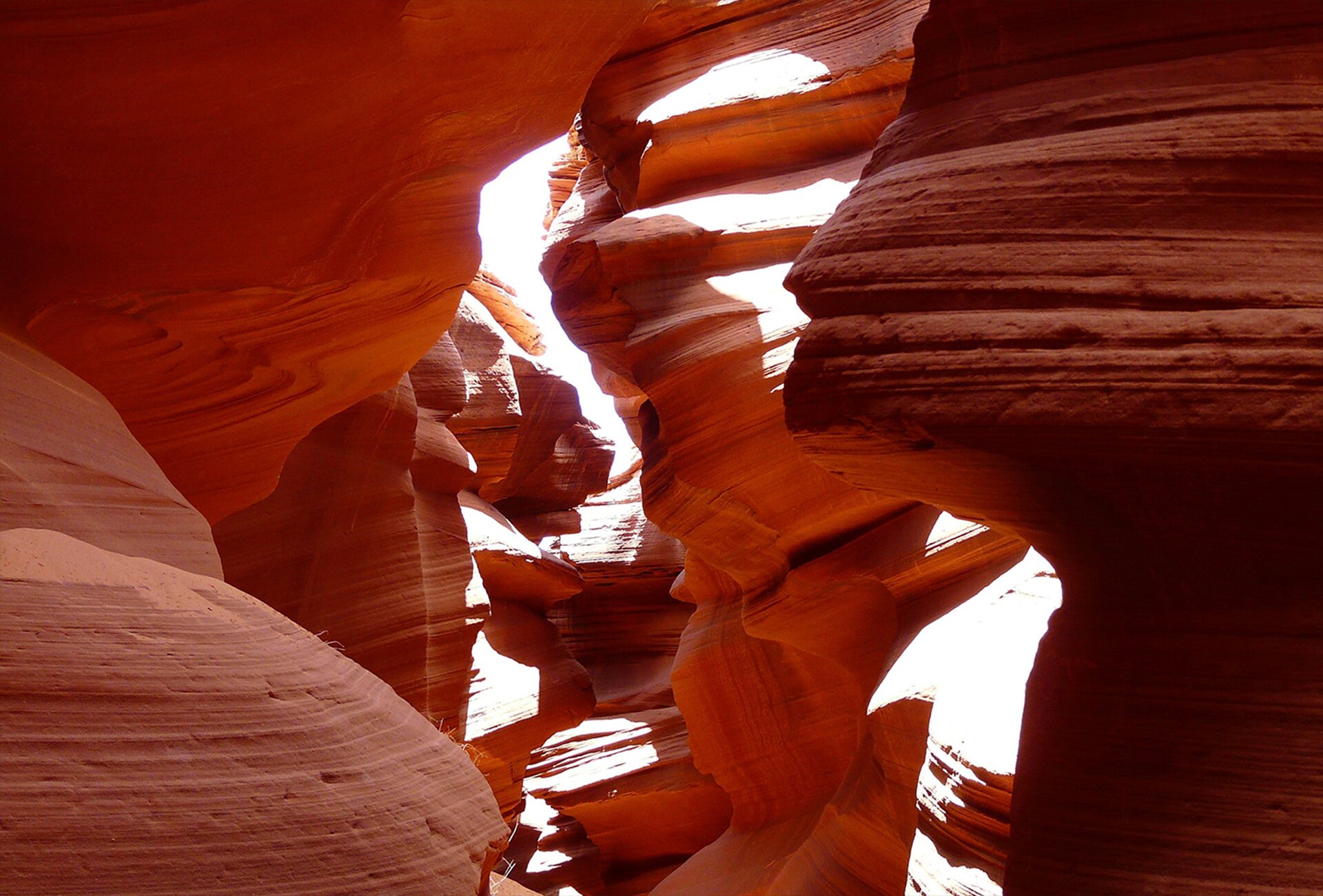 Kolorowe zdjęcie zostało wykonane wewnątrz kanionu. Widać czerwonawo-rdzawe skały o nietypowych, wygładzonych kształtach. Od góry wpadają promienie słoneczne rozświetlając wnętrze. 
