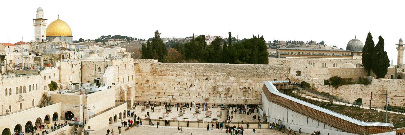 Zdjęcie współczesne, przedstawiające panoramę Ściany Płaczu w Jerozolimie, zajmuje ona centralną część fotografii. U dołu pojedyncze osoby i grupy turystów podchodzące pod obiekt lub pogrążone w modlitwie przy ścianie. Na placu przed Ścianą Płaczu rozstawione są ławki w odstępach. W lewej, górnej części fotografii widoczna złota kopuła Kopuły na Skale i sąsiadująca z nią wieża. Powyżej Ściany Płaczu widoczny zagajnik drzew. Po prawej stronie zabudowania domów, widoczna żeliwna kopuła i wieża. Na dalszym planie wzniesienia w Jerozolimie.  