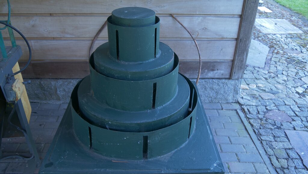 Zdjęcie przedstawia stół obręczarski. Składa się on z trzech metalowych obręczy. Obręcz przy podstawie ma największą średnicę, a obręcz przy wierzchołku najmniejszą. 