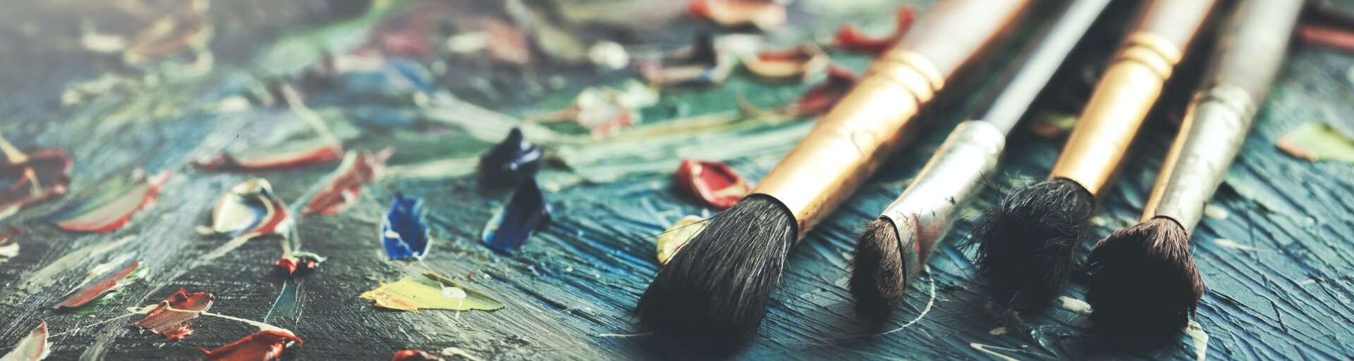 Ilustracja przedstawia cztery pędzle o różnej grubości, które leżą na zielonkawym płótnie, na którym znajdują się różnokolorowe plamy farby. Pośrodku ilustracji znajduje się pole z tytułem lekcji: "O artystach".