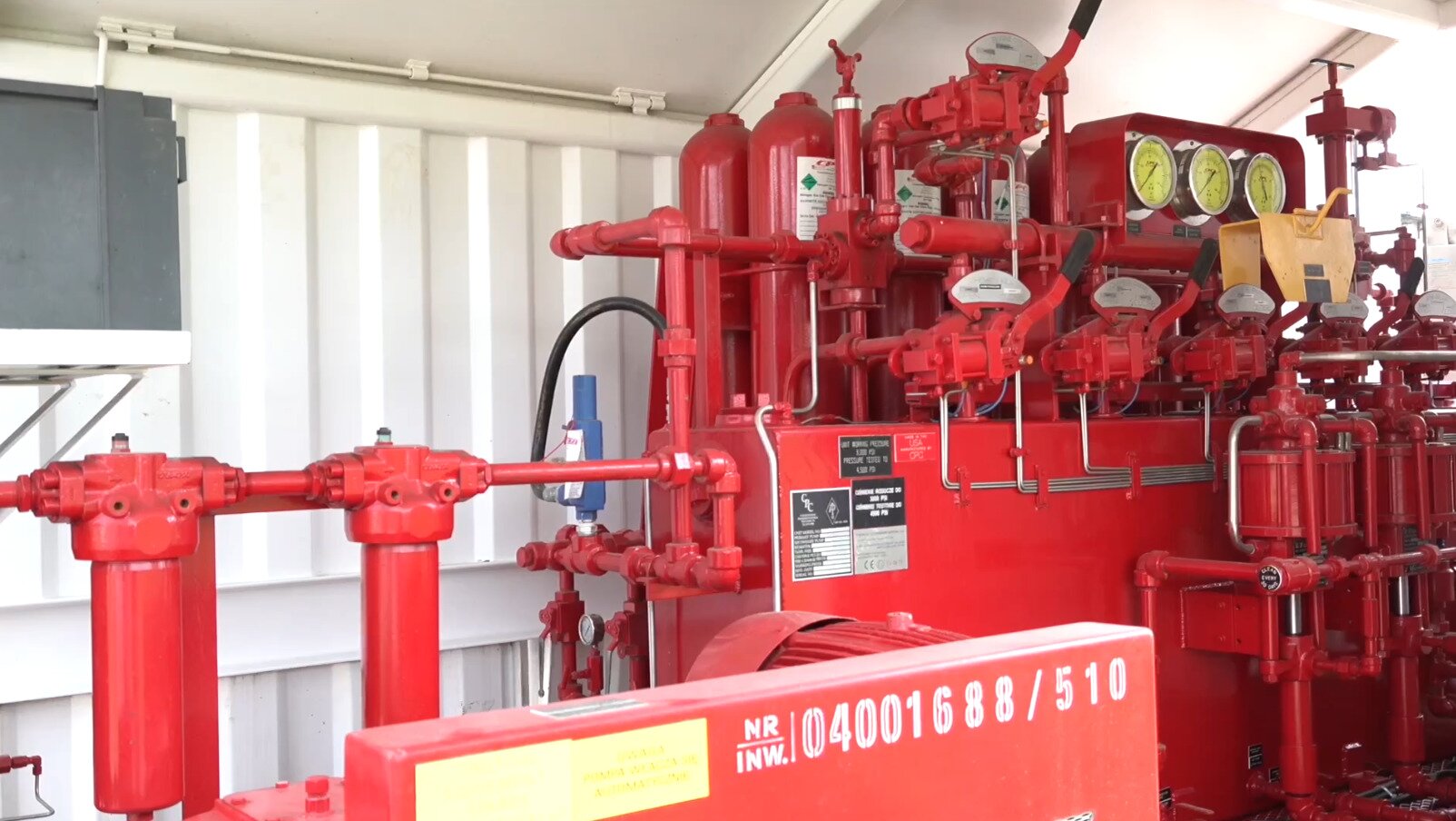 Na zdjęciu widoczna jest stacja do hydraulicznego sterowania prewenterami oraz zasuwami hydraulicznymi. Z prawej strony ekranu widoczny jest duży prostopadłościan. Wokół prostopadłościanu znajduje się duża ilość przewodów. W jego tylnej części znajdują się trzy tarcze manometrów. W jego przedniej części widocznych jest sześć dźwigni hydraulicznych. Pięć na dole i jedna w górnej części stacji. Za prostopadłościanem znajdują się elementy w kształcie butli. Z lewej strony znajduje się przyłącze do rur. W środkowej części widoczny jest fragment silnika.Poniżej zdjęcia w prawym dolnym rogu widoczny jest przycisk odtwarzania. Tekst nagrania jest zgodny z tytułem zdjęcia.