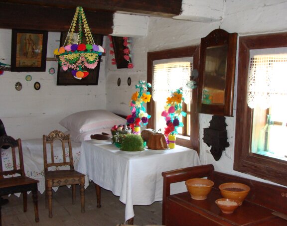 Fotografia przedstawia wnętrze chałupy chłopskiej. Dominuje drewno i oraz bielone ściany. sądząc po ozdobach, można założyć, że mieszkańcy chaty świętują Wielkanoc.