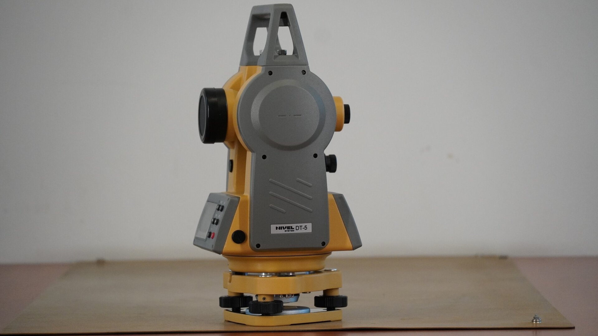 Zdjęcie ukazuje teodolit widziany z boku. Po lewej stronie znajduje się obiektyw, a po prawej okular.