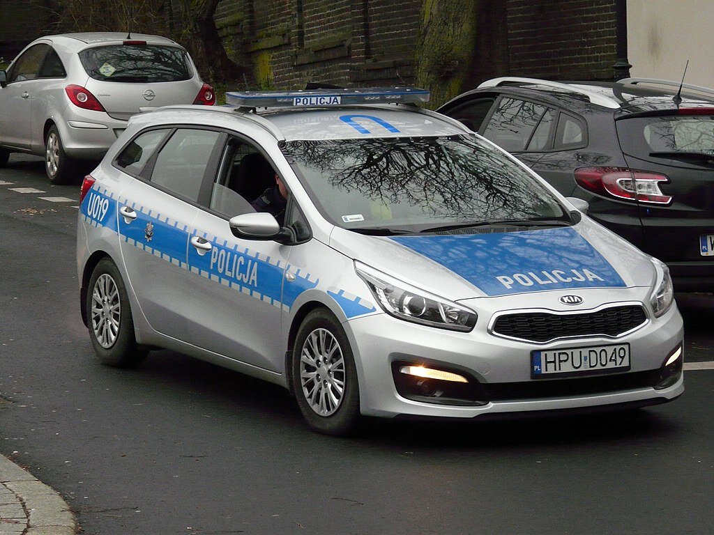 Zdjęcie przedstawia radiowóz policji. Jest to osobowy samochód marki KIA.