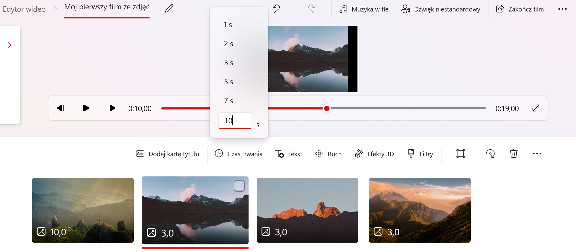 Na zrzucie ekranu przedstawiono wydłużenie czasu trwania filmu w aplikacji Edytor Wideo. Ekran roboczy aplikacji jest podzielony na dwie sekcje. W górnej części znajduje się ścieżka z wybranymi zakładkami: edytor wideo, mój pierwszy film ze zdjęć. Za nią widoczny jest przycisk z rysunkiem ołówka. Po prawej stronie aplikacji widoczne są przyciski: strzałka z grotem skierowanym w lewo, strzałka z grotem skierowanym w prawo, muzyka w tle, dźwięk niestandardowy, zakończ film i trzy kropki rozwijające więcej opcji.Poniżej widoczne jest okno edycji filmu. Główną cześć okna stanowi prostokątny obszar na którym wyświetlany jest film. Przykładowo jest to klatka filmowa pokazujący górzysty teren porośnięty drzewami. Pod obszarem filmowym umieszczony jest suwak pokazujący czas trwania. Na suwaku jest okrągły znaczki czasu.Po lewej stronie suwaka znajduje się przycisk z narysowanym grotem strzałki skierowanym w lewo, przycisk , przycisk z narysowanym grotem zwróconym w prawo oraz informacja o czasie trwania filmu. Z prawej strony suwaka widoczna jest informacja z czasem trwania filmu praz przycisk przedstawiający prostą na końcu której znajdują się groty strzałek. Groty są skierowane na zewnątrz.Pod suwakiem znajduje się sekcja: scenorys. W sekcji scenorysu widoczne są cztery obrazy przedstawiające tereny górskie. W lewym dolnym rogu obrazów znajduje się cyfry. Pierwszy obraz ma cyfrę dziewięć pozostałe trzy obrazy mają cyfrę trzy.W prawym górnym rogu sekcji scenorysu umieszczone są przyciski: dodaj kartę tytułu, czas trwania, tekst, ruch, efekty trzy de, filtry, przycisk z symbolem prostokąta w narożach którego znajdują się okręgi, przycisk z symbolem punktu wokół którego prowadzona jest strzałka której grot skierowany jest w dół, przycisk kosza, oraz trzy kropki po naciśnięciu których pojawia się więcej opcji. Po naciśnięciu przycisku czas trwania rozsuwa się  menu kontekstowe. Kolejne opcje: jedna sekunda, dwie sekundy, trzy sekundy, pięć sekund, siedem sekund, okno z dowolnym czasem do wpisania. Przykładowo dziesięć sekund. Opcja ta jest wybrana. Widoczna jest zmiana czasu na pierwszym obrazie.