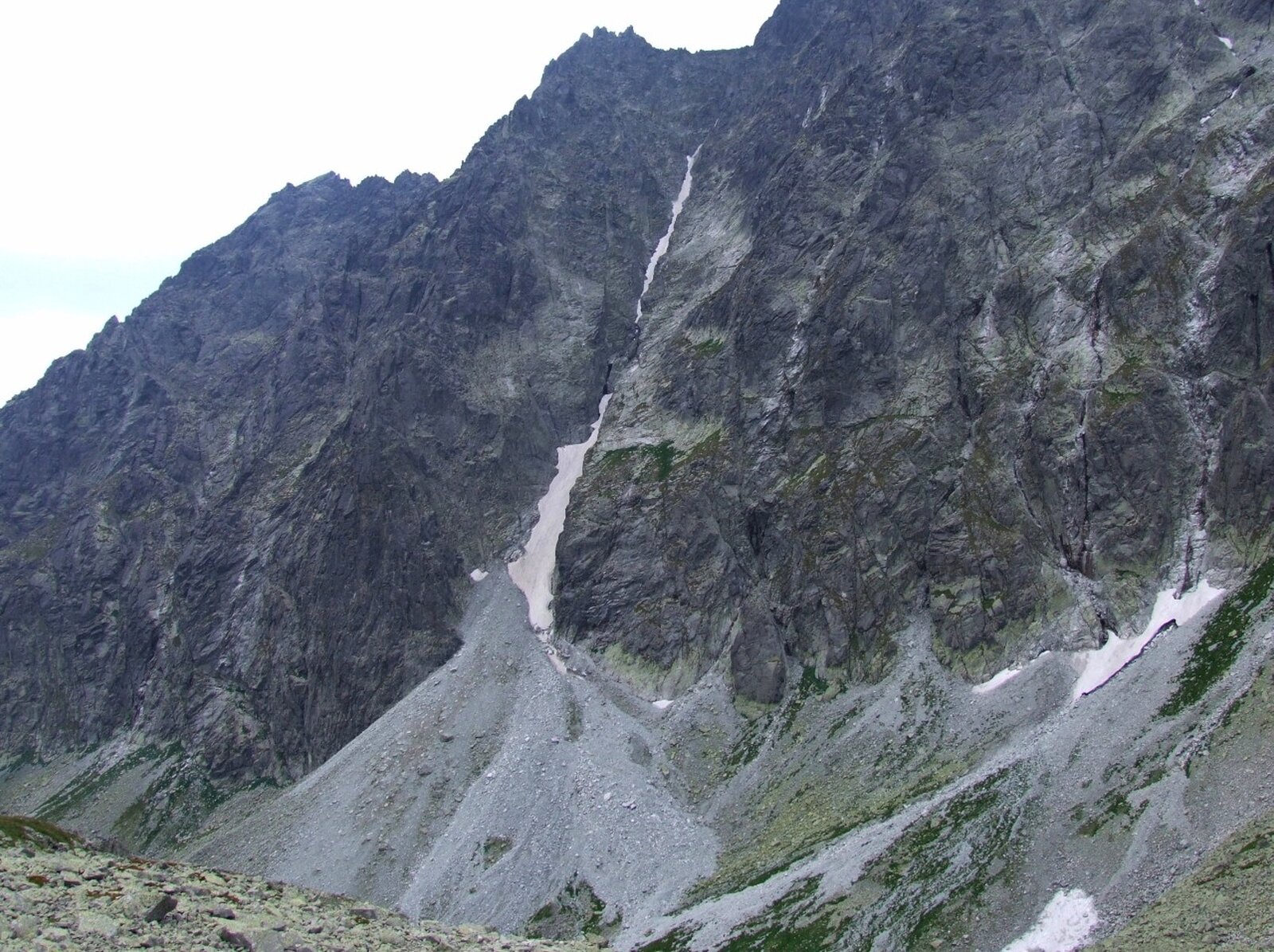 Stromy stok góry. Pośrodku niego znajduje się żleb, czyli podłużne, pionowe wcięcie w jego ścianie. U podnóża szczeliny mieści się piarg, czyli nagromadzenie drobnego materiału skalnego. Piarg tworzy kształt stożka, zebrany materiał ma szary kolor, nieco jaśniejszy od stoku powyżej.