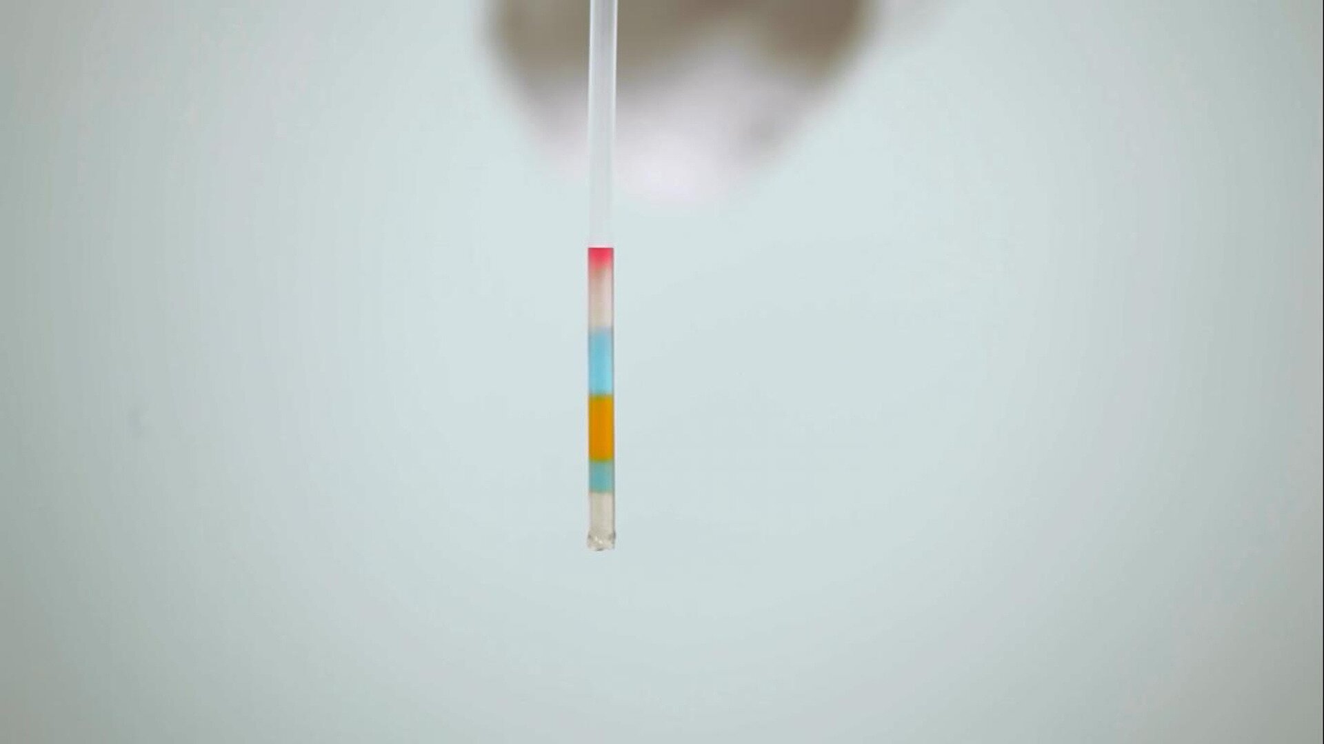 Fotografia przedstawia pipetę (transparent straw) napełnioną roztworami z różnymi barwnikami, różnokolorowe roztwory wyraźnie są oddzielone od siebie, niezmieszane.