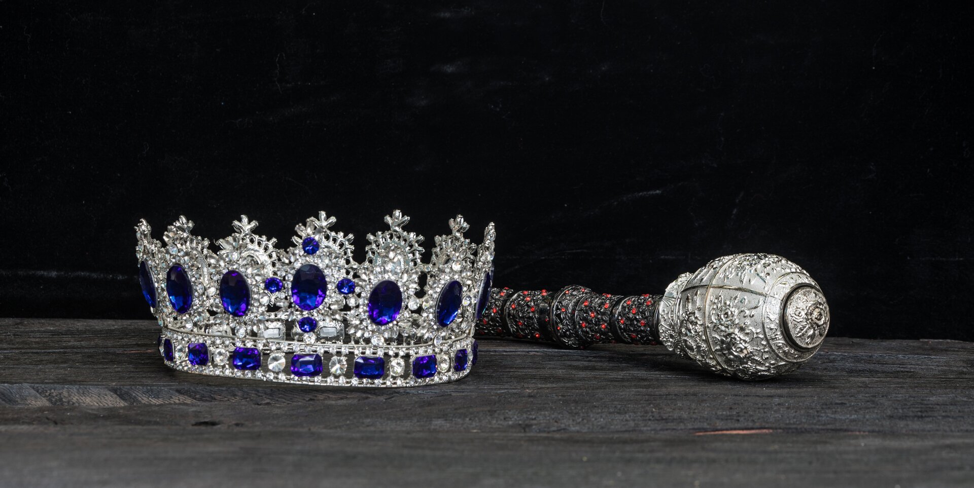 Zdjęcie przedstawia srebrną koronę królewską wysadzoną drogocennymi klejnotami oraz berło królewskie.