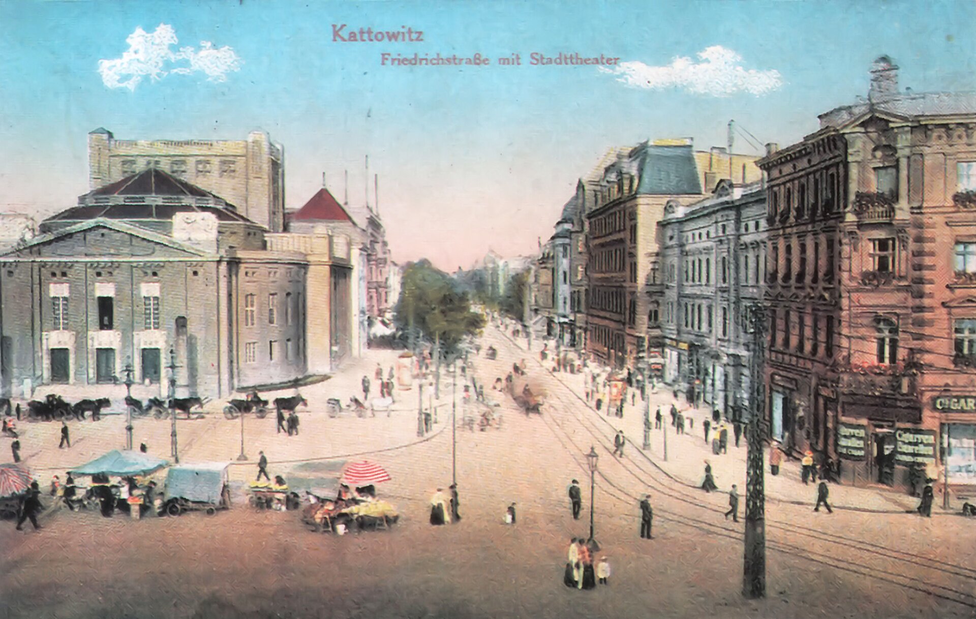 Zdjęcie przedstawia fragment miasta. Szeroka ulica, na której są też tory tramwajowe, krzyżuje się z inną ulicą na dużym placu, gdzie po lewej stronie na pierwszym planie stoją stragany. Po obu stronach ulicy stoją wysokie kamienice. Po ulicy jadą bryczki zaprzężone w konie, widać również stojących i idących przechodniów.