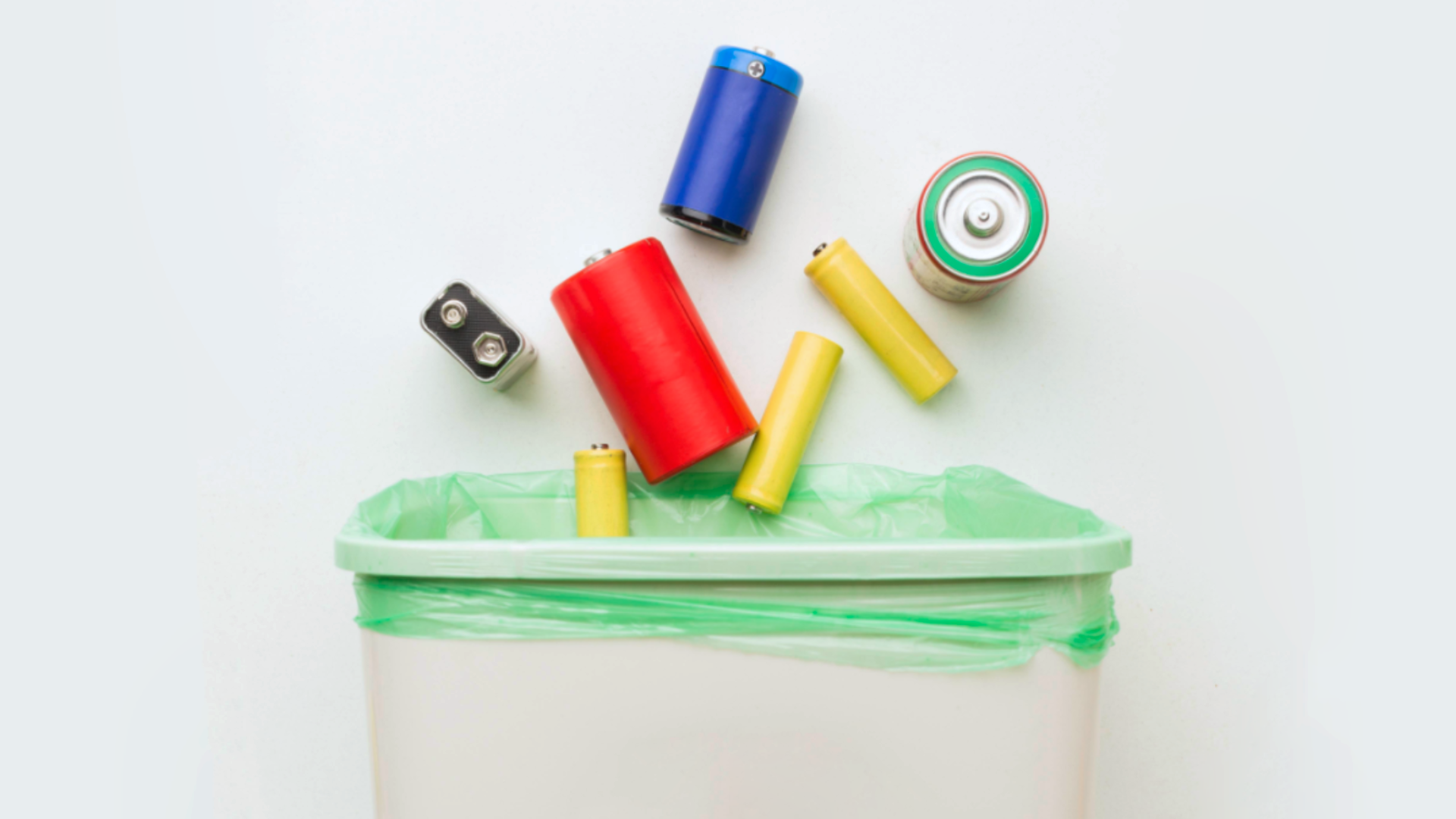 Zdjęcie przedstawia różne rodzaje zużytych  baterii, które wpadają do kosza.