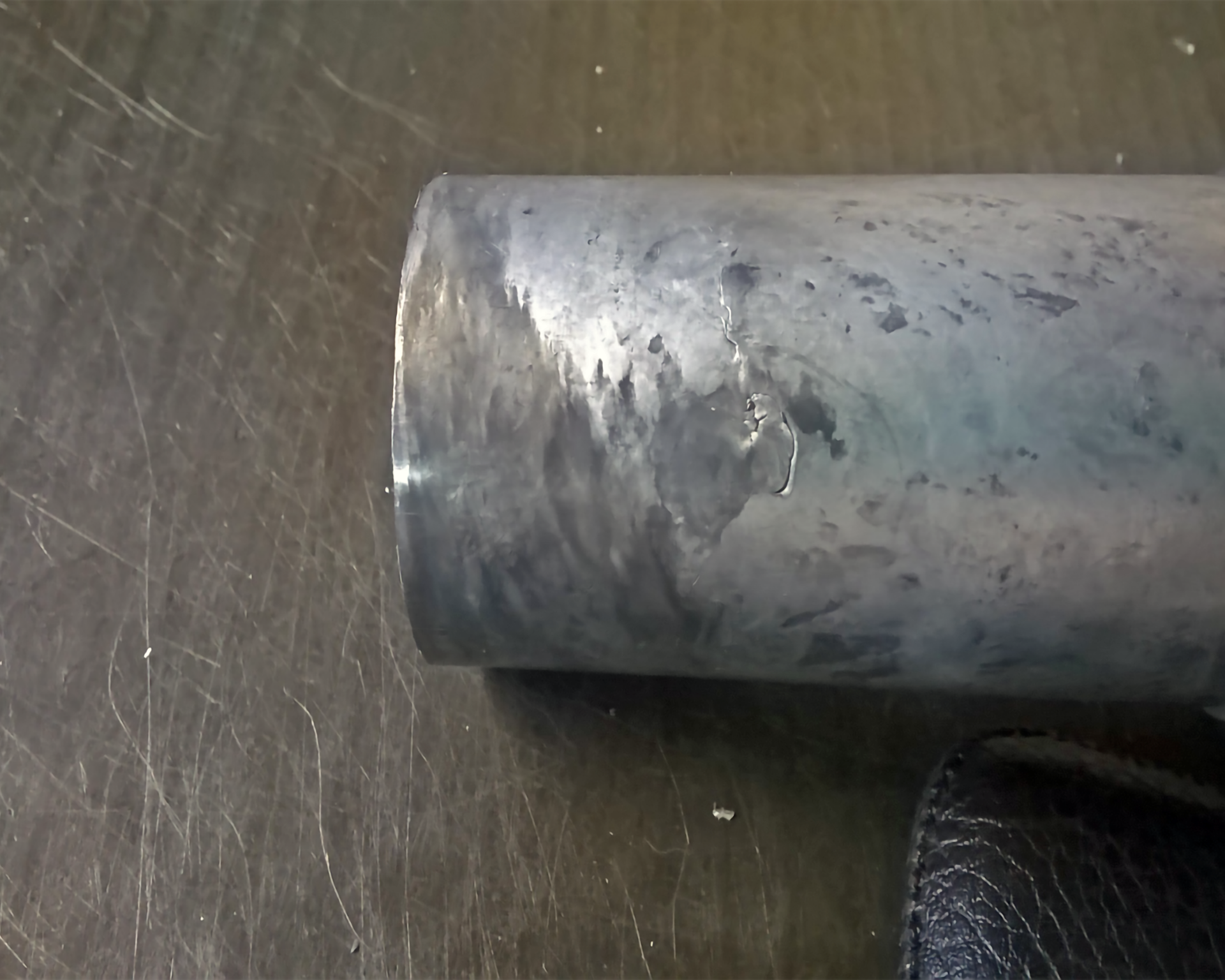 Zdjęcie przedstawia przybliżony, walcowaty, metalowy element. Posiada on niespaw, czyli pęknięcie na powierzchni.