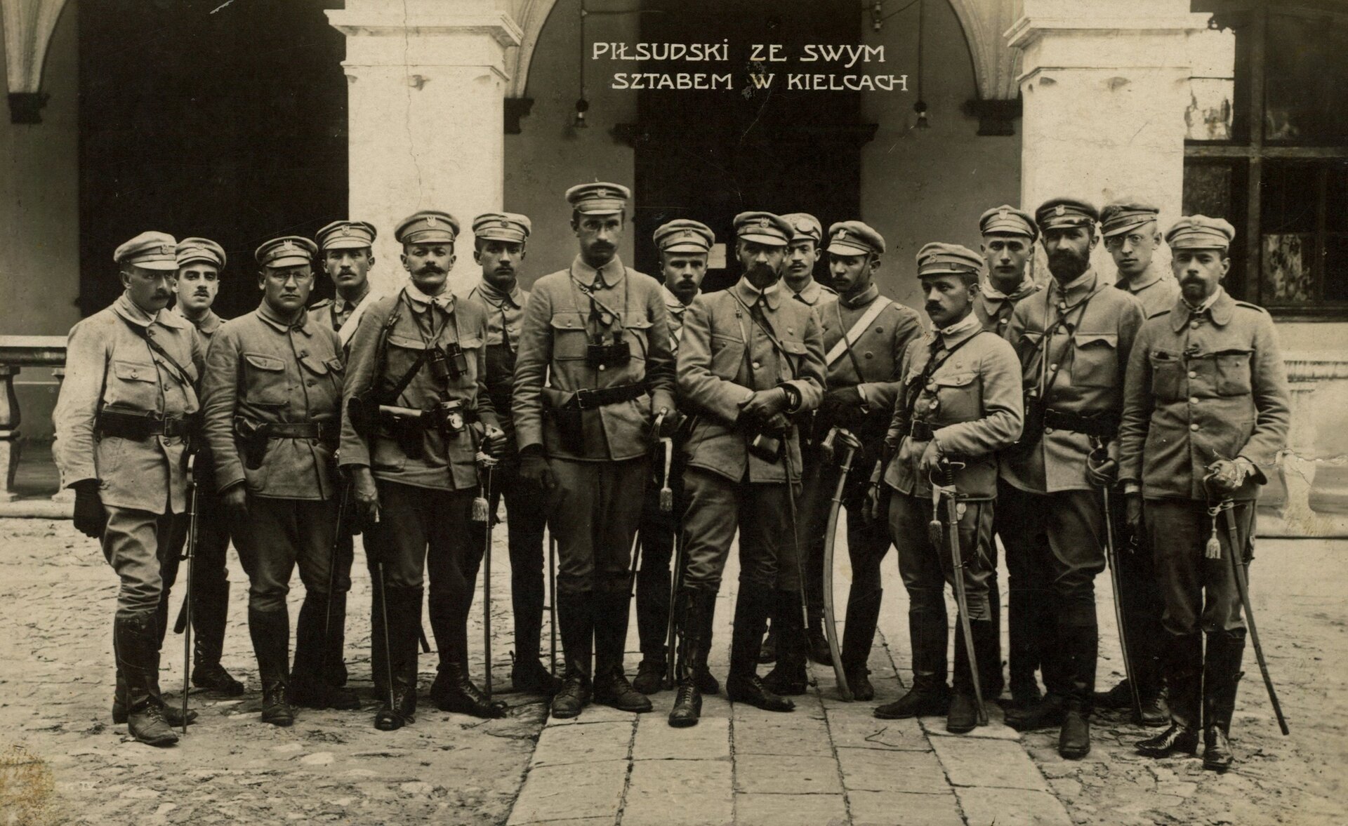 Pułkownik Józef Piłsudski (po środku) ze swoim sztabem przed Pałacem Gubernialnym w Kielcach, 1914 rok. Oddział 6 sierpnia 1914 roku wyruszył z Krakowa w kierunku Kielc, dotarł tam 12 sierpnia. Tego samego dnia doszło do pierwszych strać z wojskami carskimi. W co są uzbrojeni żołnierze widoczni na zdjęciu?