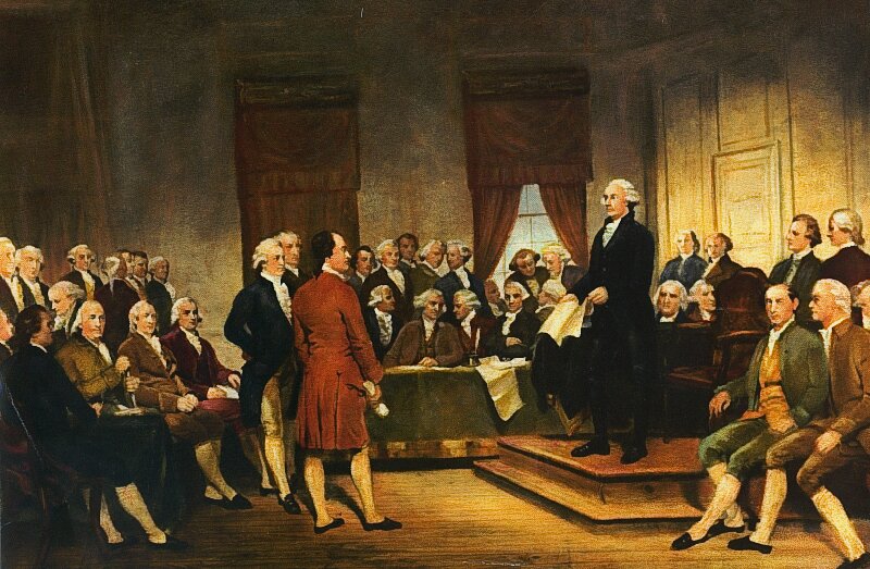 Obraz przedstawia grupę meżczyzn w pomieszczeniu, siędzą lub stoją. Jeden z nich, stojący pokazuje pozostałym dokument.