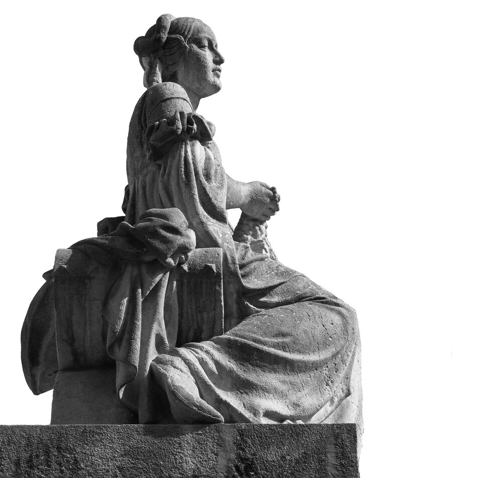 Na zdjęciu rzeźba siedzącej kobiety z upiętymi włosami pod czepkiem. Jest ubrana w suknię z marszczonymi rękawami. W prawej ręce trzyma skrawek szaty. Jej prawa noga jest zgięta w kolanie. Kobieta patrzy przed siebie. Za jej plecami leży zwinięta szata.