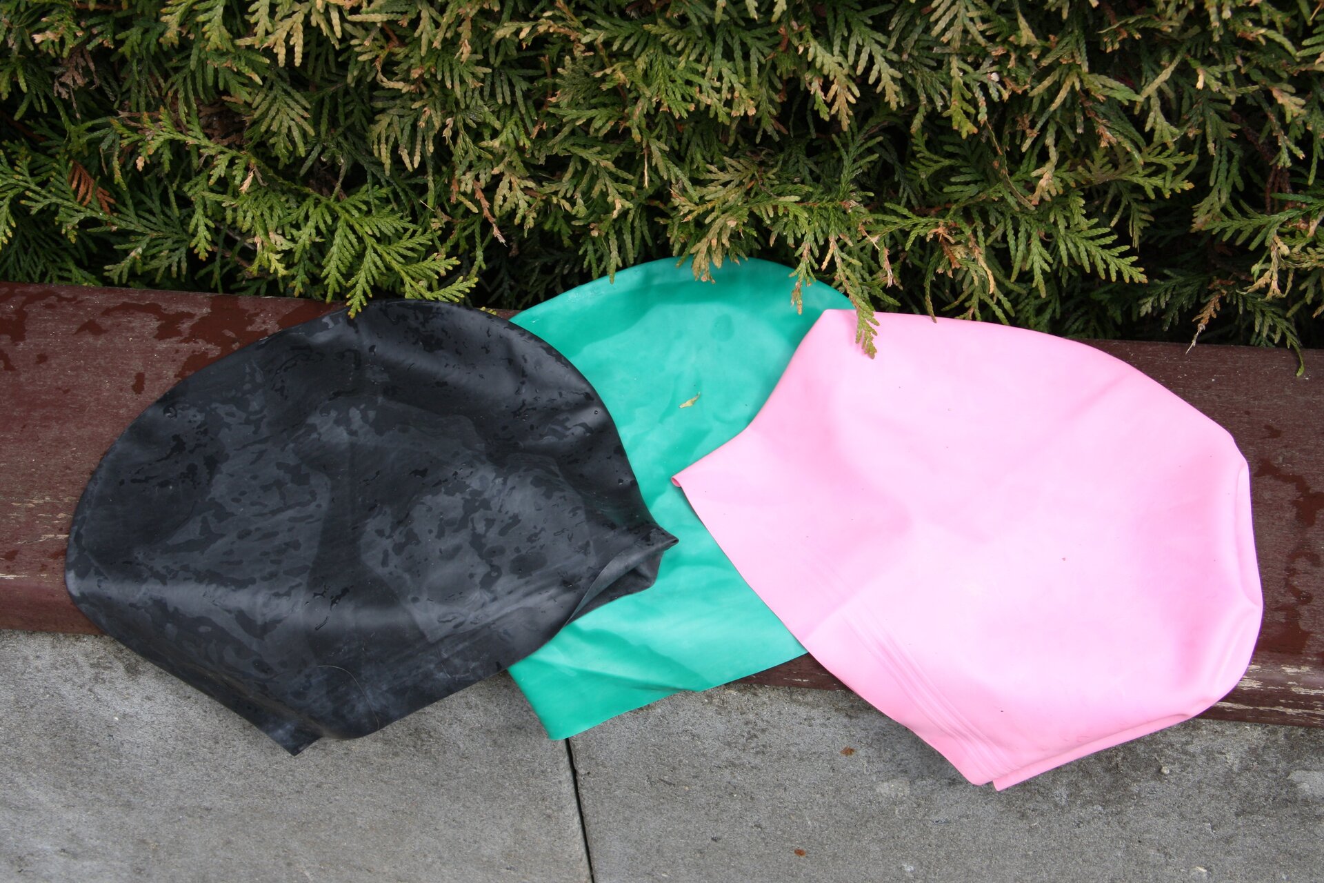 Ilustracja przedstawia trzy czepki kąpielowe w kolorach czarnym, zielonym i różowym.